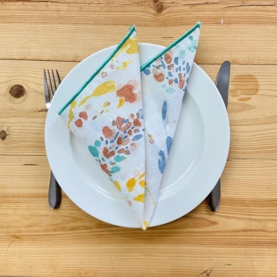 Guardanapos coloridos sobre prato branco numa mesa de madeira com talheres