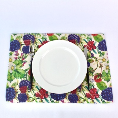 Prato branco com garfo e faca sobre placemat com padrão de frutas coloridas.