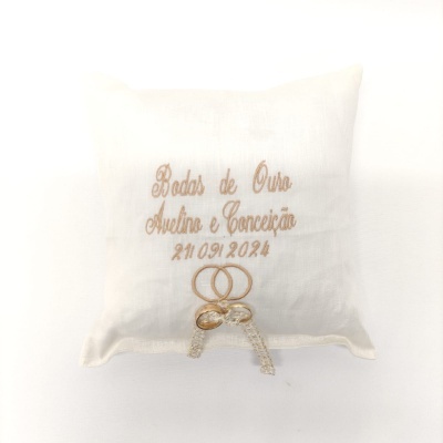 Almofada branca bordada com texto dourado e decoração de anéis e laço de renda