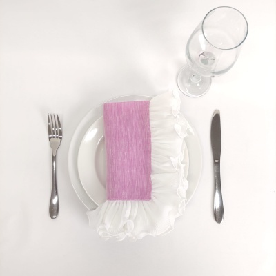 Mesa posta com prato branco, guardanapo rosa e branco, talheres metálicos e copo de vidro.