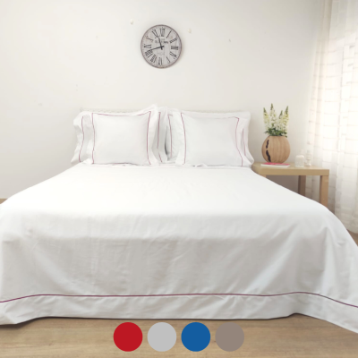 Cama com roupa de cama branca com costura vermelha, relógio de parede e mesa de cabeceira com vaso