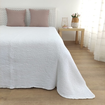 colcha branca com padrão trançado, almofadas cor de rosa, mesa de cabeceira com vaso de flores