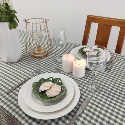 Mesa de jantar posta com toalha xadrez verde e branca, pratos e copos, velas e decoração.