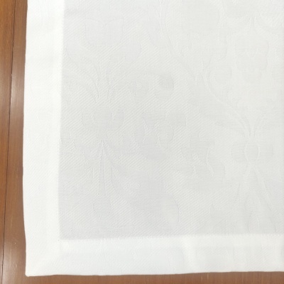 Toalha branca com padrão floral em relevo e borda sólida sobre mesa de madeira clara