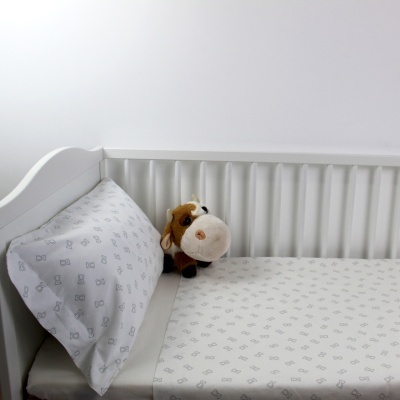 Cama de criança branca com lençóis brancos com padrão cinza e peluche de vaca.