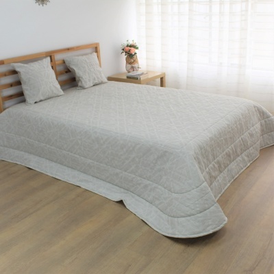 Colcha e almofadas cinza com padrão geométrico em cama de madeira clara num quarto luminoso