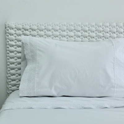 Almofada branca bordada sobre cama com cabeceira trançada branca