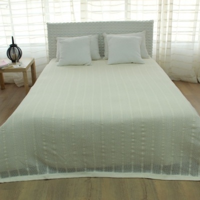 Cama branca com colcha e almofadas brancas, mesa de cabeceira com candeeiro preto