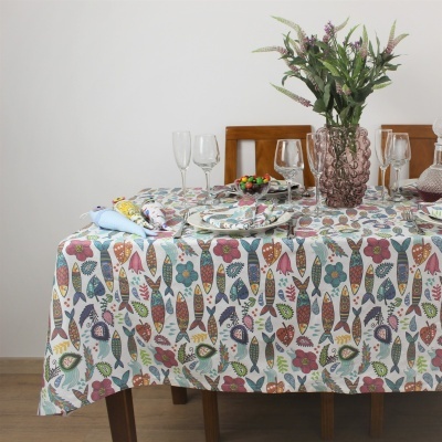 Mesa com toalha colorida estampada, pratos, copos, vaso rosa com flores e cadeira de madeira.