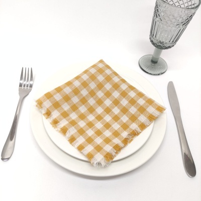 Mesa posta com prato branco, guardanapo xadrez amarelo e branco, talheres metálicos e copo cinza