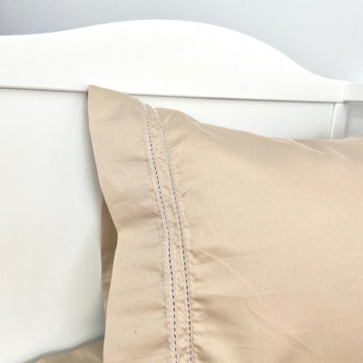 Travesseiro com fronha bege e costura decorativa numa cama com cabeceira branca