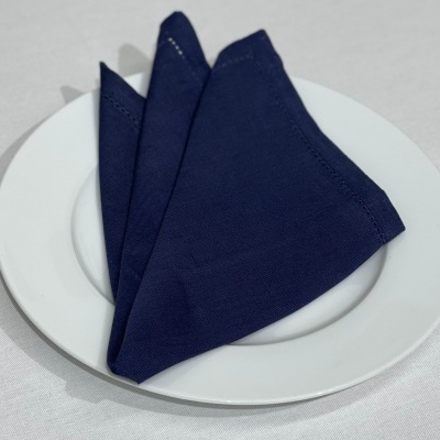 Guardanapo azul escuro dobrado em prato branco sobre toalha branca