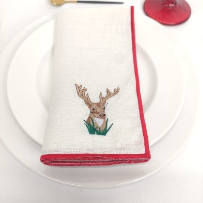 Guardanapo branco com borda vermelha e bordado de veado sobre prato branco
