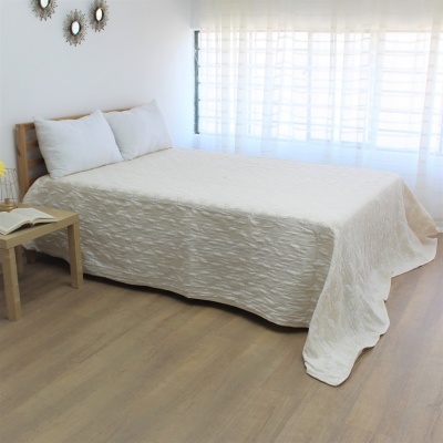 Cama com colcha branca texturizada e almofadas em quarto minimalista