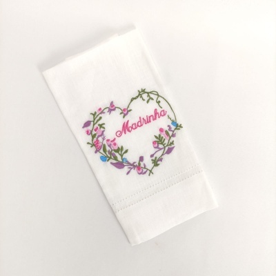 Guardanapo branco bordado com coração de flores e a palavra 'Madrinha' no centro