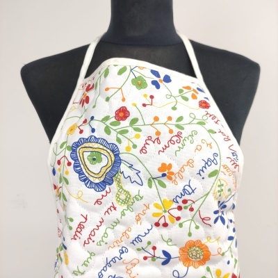 Avental branco com padrão floral colorido e texto bordado em manequim preto