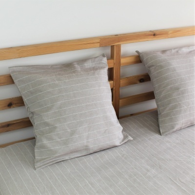 Dois almofadas e cama com tecido riscado bege e branca, cabeceira de madeira clara