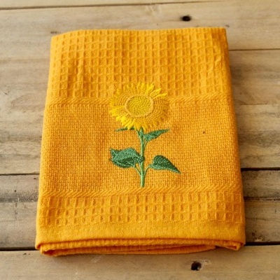 Toalha amarela com bordado de girassol sobre madeira