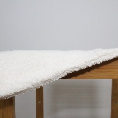 Toalha branca felpuda pendurada numa estrutura de madeira clara.