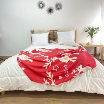 Cobertor vermelho com renas e estrelas sobre cama branca em quarto minimalista