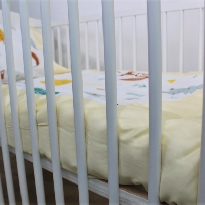 Berço branco de madeira com colchão amarelo e cobertor colorido