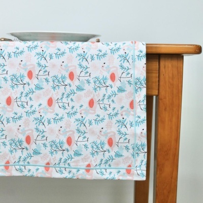 Pano de prato branco com padrão floral azul e rosa pendurado numa mesa de madeira