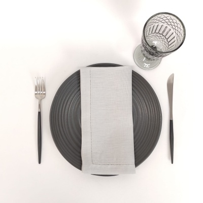 Conjunto de jantar com prato cinzento, guardanapo bege, talheres pretos e copo de vidro