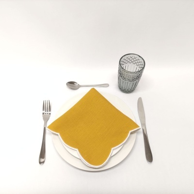 Conjunto de jantar com prato branco, guardanapo amarelo, talheres em metal e copo de vidro