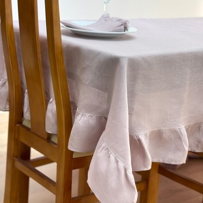 Toalha de mesa rosa claro com acabamento ondulado sobre mesa de madeira clara com prato, guardanapo e copo