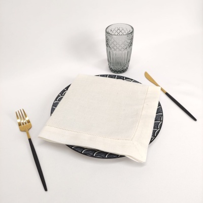 Mesa posta com prato decorativo, guardanapo branco, talheres preto e dourado e copo de vidro com relevo.