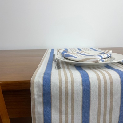 Toalha de mesa com riscas azuis, bege e brancas, prato branco e garfo numa mesa de madeira
