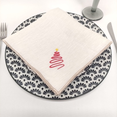 Guardanapo branco com bordado de árvore de Natal sobre prato com padrão preto e branco