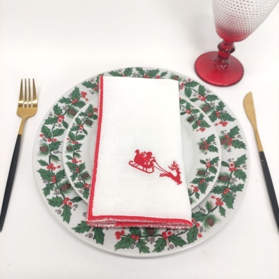 Pratos decorados com padrão natalício, guardanapo branco e talheres dourados com cabo preto em fundo branco