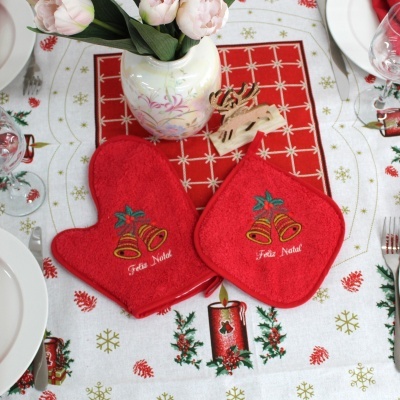 Jogo de forno vermelho com bordado de sinos e frase Feliz Natal sobre mesa decorada para Natal