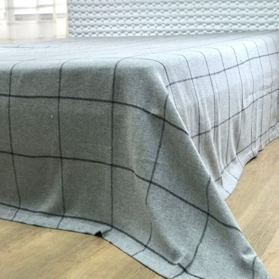 Cama com colcha cinzenta de padrão de grades em chão de madeira clara