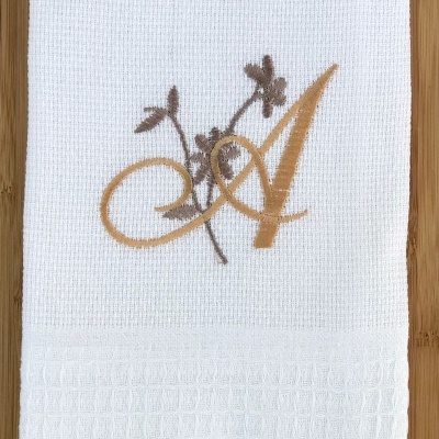Toalha branca com bordado letra A e ramo floral sobre madeira