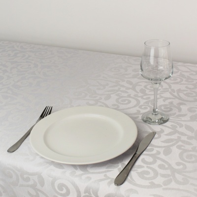 Conjunto de mesa com toalha branca, prato branco, talheres de metal e copo de vinho de vidro