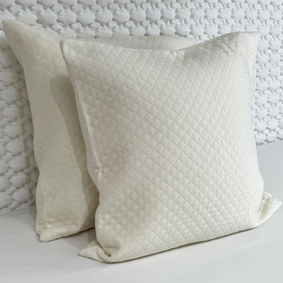 Duas almofadas creme com padrão em losangos na frente de parede texturizada branca