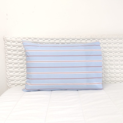 Travesseiro azul com riscas finas numa cama branca matelassada