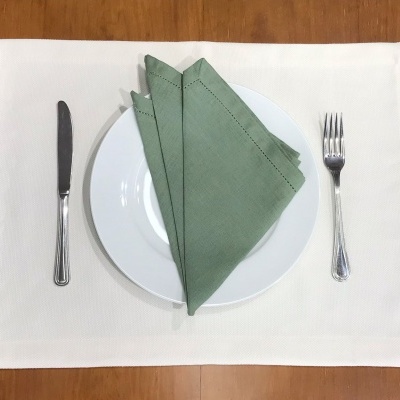 Mesa posta com prato branco, guardanapos verdes e talheres sobre base branca