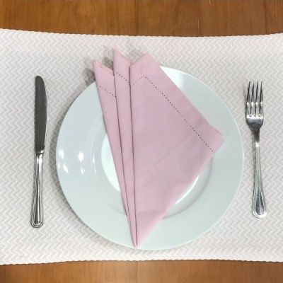 Prato branco com guardanapos cor-de-rosa e talheres sobre toalhete bege e mesa de madeira