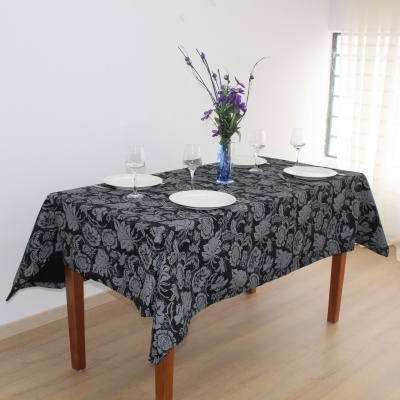 Mesa de jantar com toalha preta com padrão floral cinzento, pratos, copos e vaso com flores