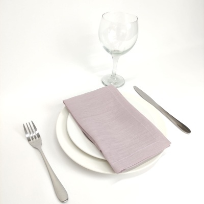 Conjunto de louça branco, talheres prateados, guardanapo rosa claro e copo de vidro