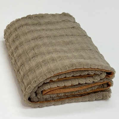 Toalha ou manta texturizada bege e interior laranja dobrada sobre fundo branco