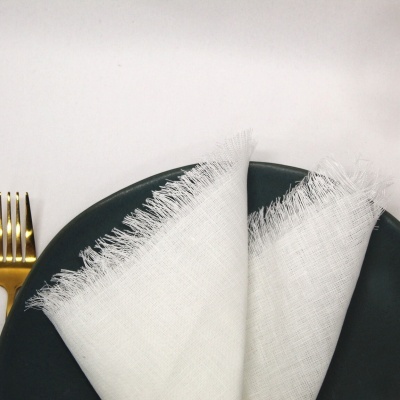 Guardanapo branco franjado em prato preto com garfo dourado