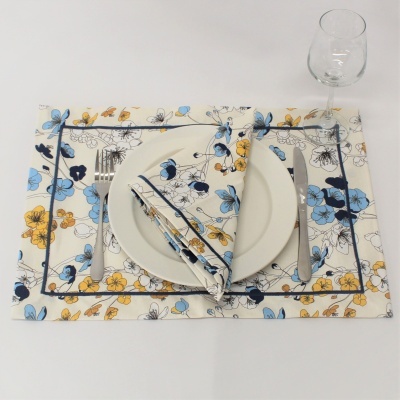 Jogo americano e guardanapo com padrão floral azul e amarelo, talheres de metal e copo de vidro