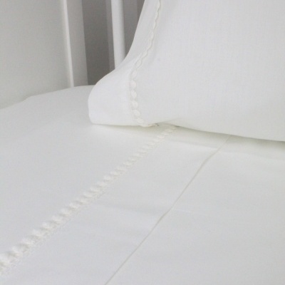 Lençóis brancos com bordado decorativo numa cama com estrutura de metal branca