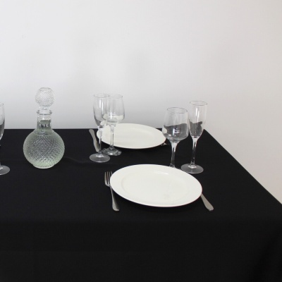 Mesa posta com loiça branca, copos de vidro e decanter sobre toalha preta