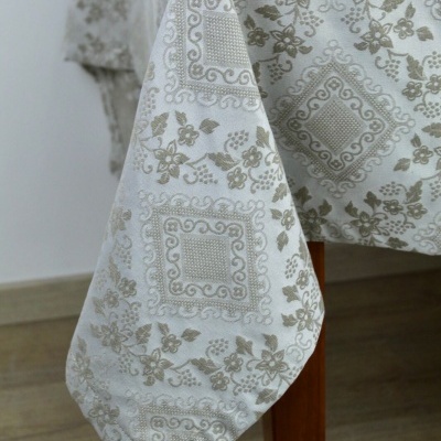 Toalha de mesa branca com padrão floral bege pendurada numa mesa de madeira.