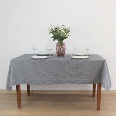 Mesa com toalha cinza, vaso rosa com flores, pratos brancos e copos de vidro
